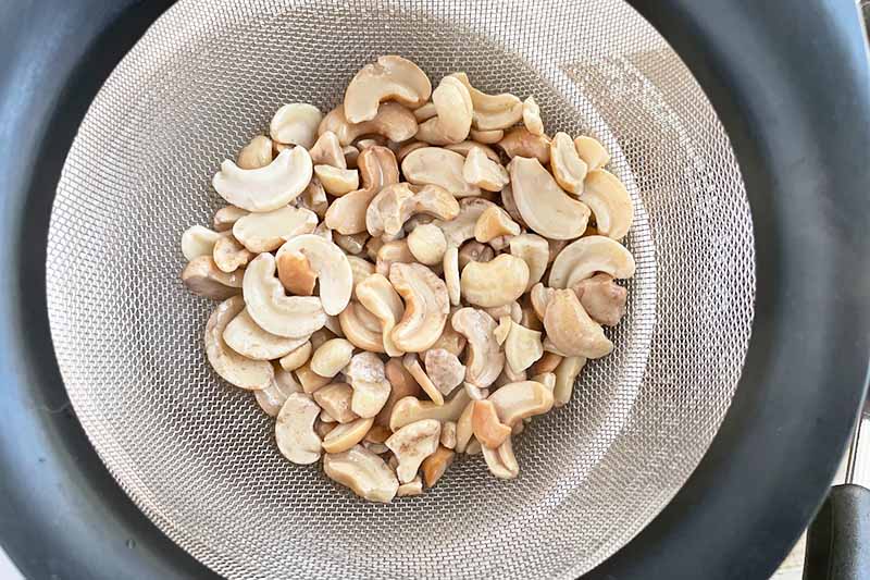 Horizontal image of soaked cashews in a strainer.