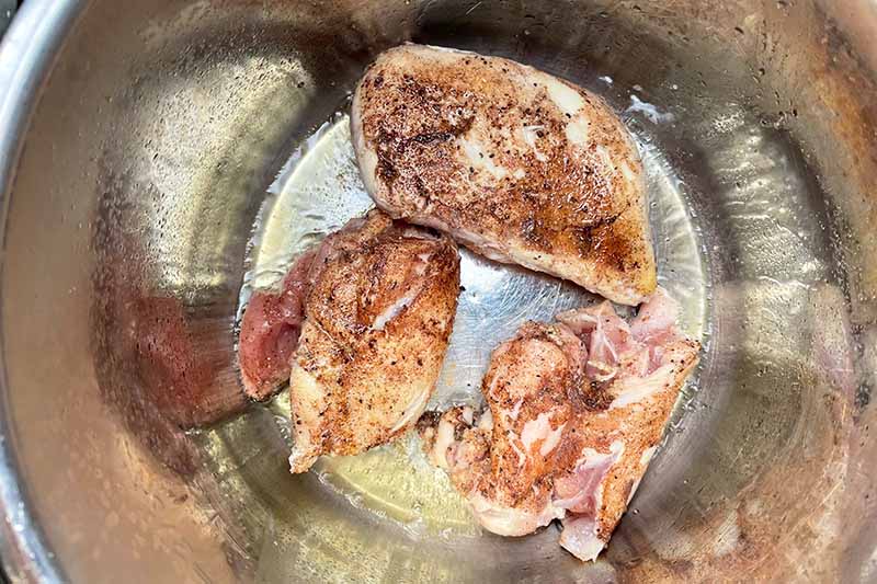 Horizontal image of searing pieces of raw poultry in a pot.