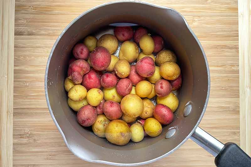 Horizontal image of boiling whole baby potatoes in a pot.