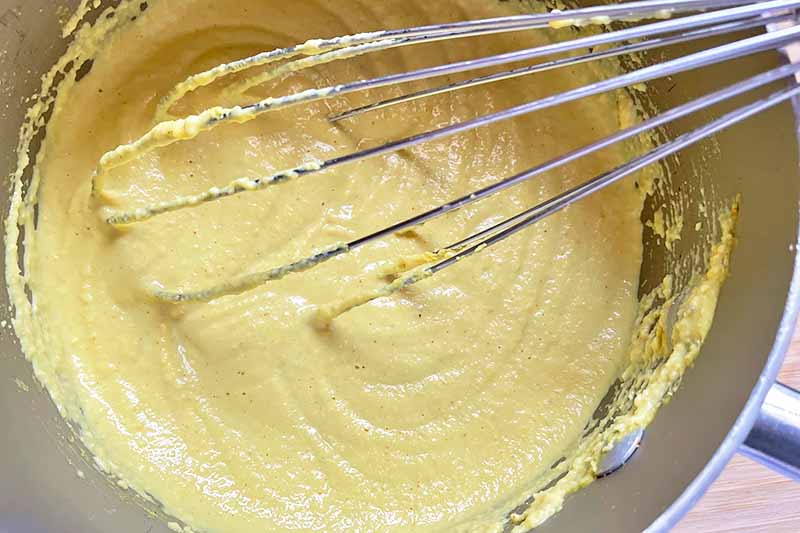 Horizontal image of whisking a thick yellow mixture in a pot.