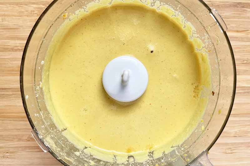 Horizontal image of a thick yellow liquid mixture in a food processor.