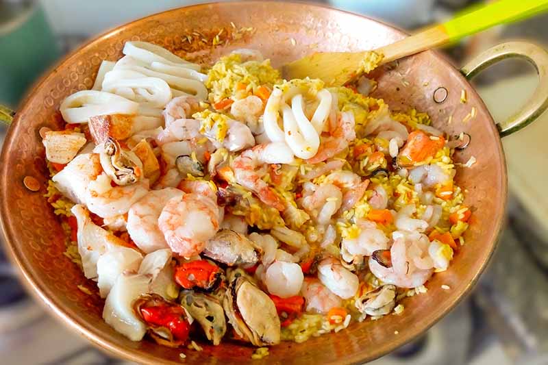 Horizontal image of copper cookware with rice and assorted seafood.