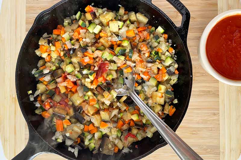 Horizontal image of cooking an assortment of chopped vegetables in a cast iron skillet.