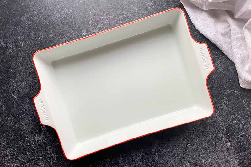 Horizontal top-down image of an empty white porcelain cookware with red rim on a black background.
