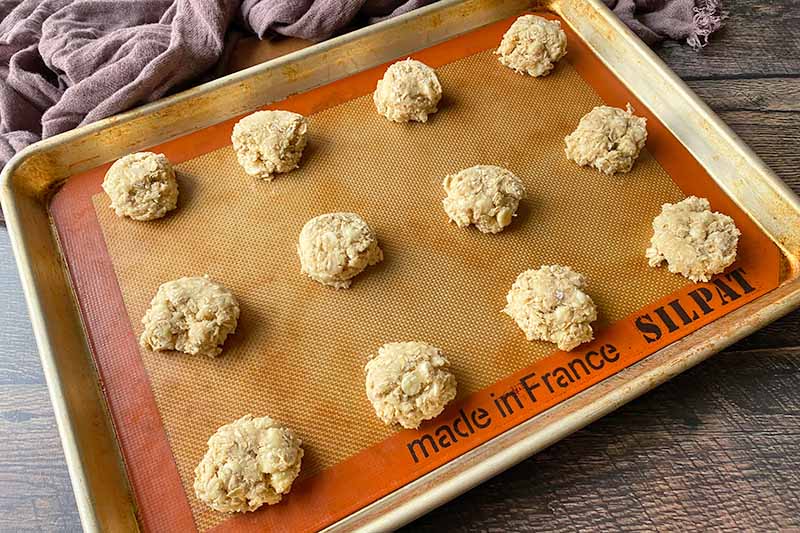 Horizontal image of portioned mounds of dough on a baking sheet lined with a silicone mat.