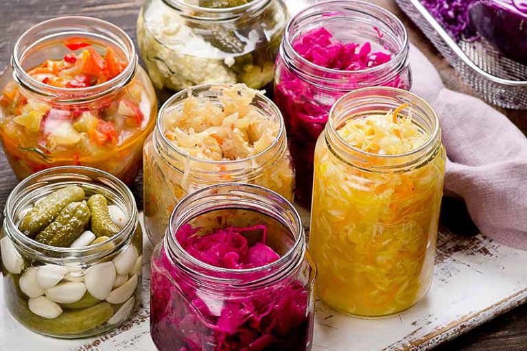 Horizontal image of jars of assorted fermented vegetables on a towel.