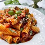 Horizontal image of a pasta and tomato sauce recipe in a white bowl on top of blue napkins.