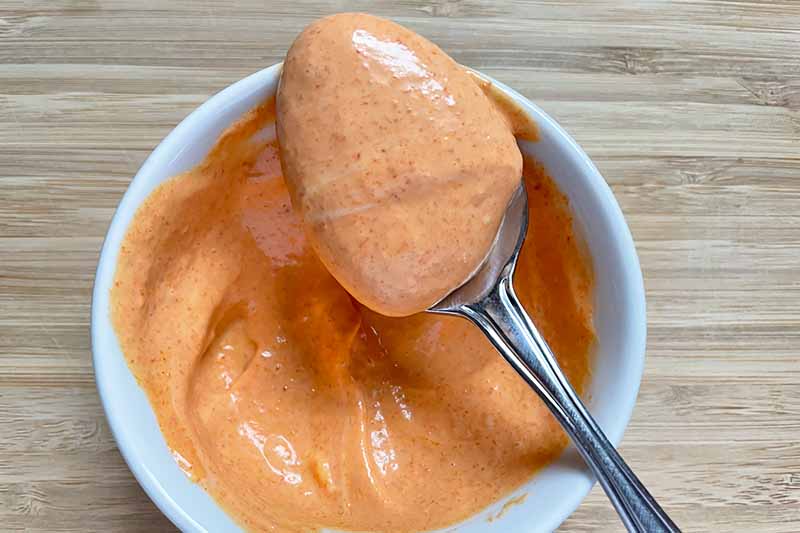 Horizontal image of a red mayo-based sauce on a spoon over a bowl.