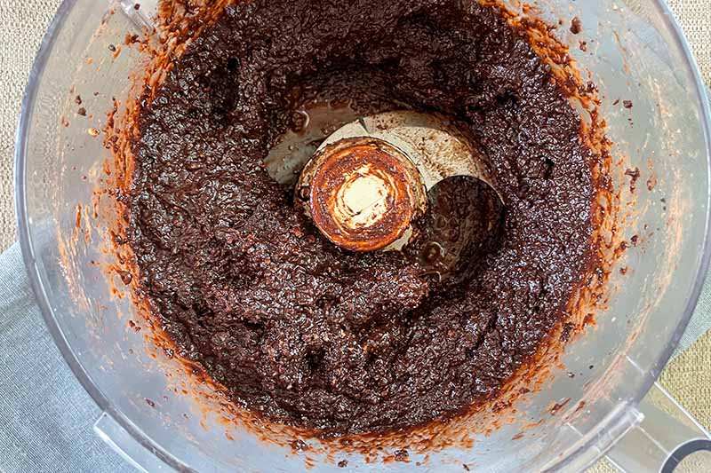 Horizontal image of a brown paste in a food processor.