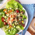 Horizontal image of a white plate with bib lettuce and a seafood and vegetable mixture on a blue napkin.