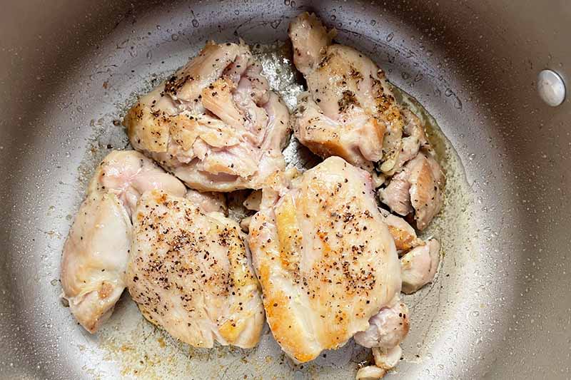 Horizontal image of searing chicken thighs in a pot.