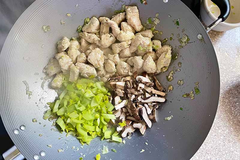 Horizontal image of chunks of meat, celery, and mushrooms cooking in a wok.