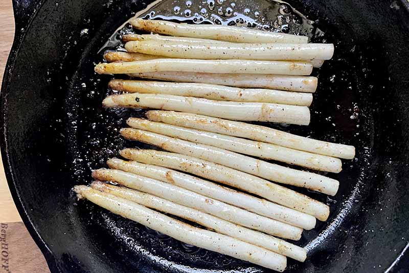 Horizontal image of cooking white stalk vegetables in a cast iron skillet.