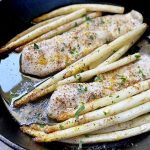 Horizontal image of baked fish fillets and white vegetables in a cast iron skillet.