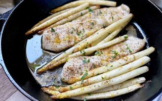 Horizontal image of baked fish fillets and white vegetables in a cast iron skillet.