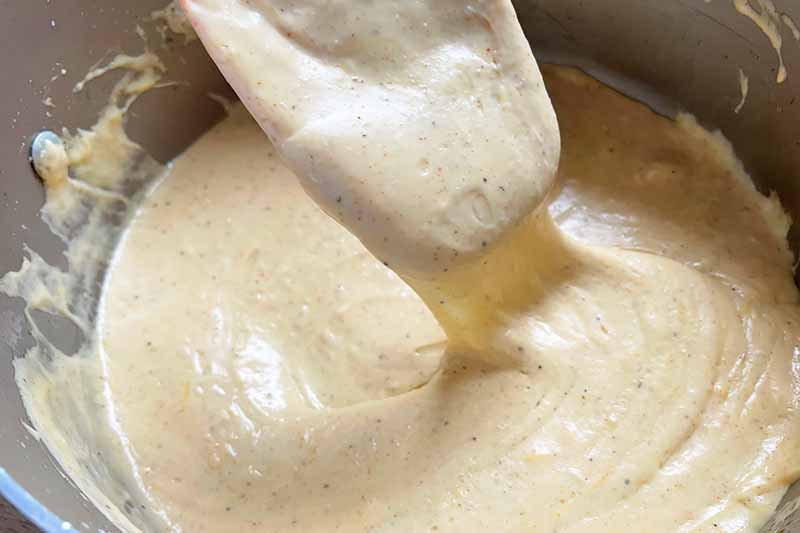 Horizontal image of stirring a thick and gooey cream sauce in a pot.