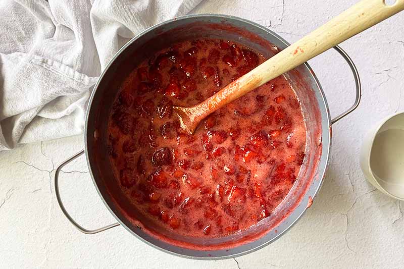 Horizontal image of using a wooden spoon to stir a thick bright red mixture in a pot.