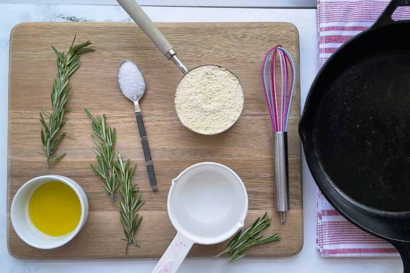Horizontal image of dry and wet ingredients and sprigs of rosemary on a cutting board.