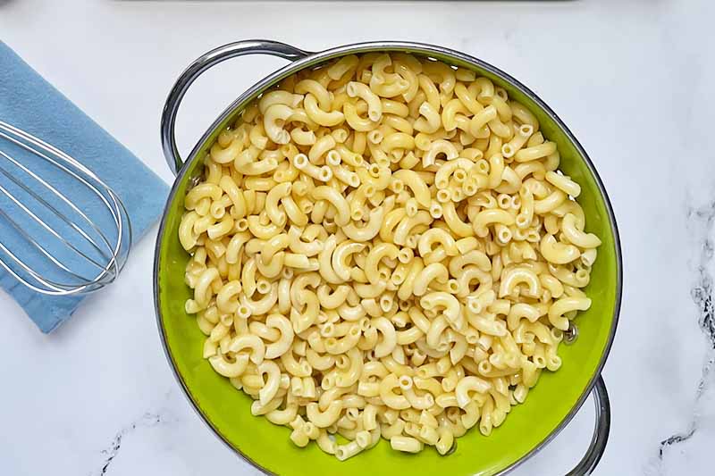 Horizontal image of draining cooked pasta in a green colander.