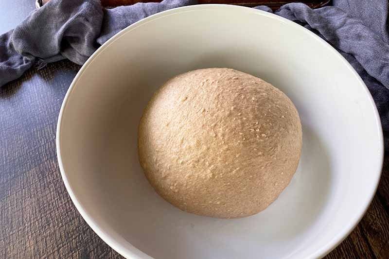Horizontal image of a round light brown dough in a white bowl.