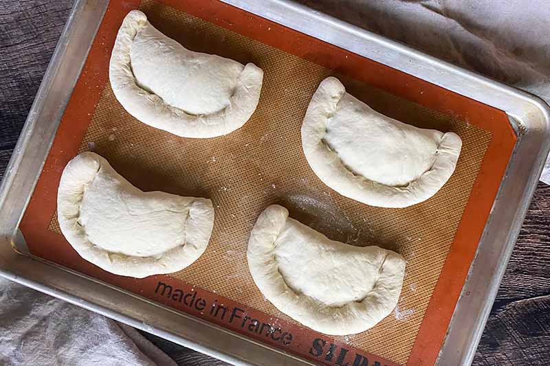 Horizontal image of unbaked calzones on a pan.