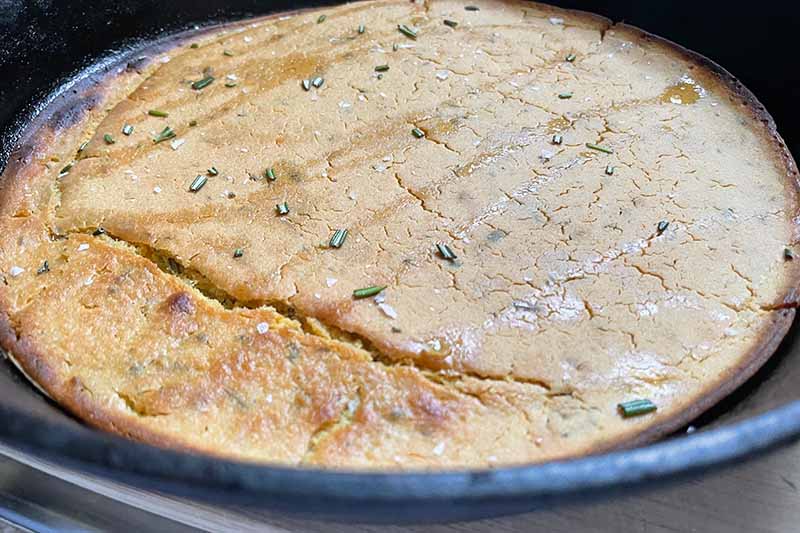 Horizontal image of a baked herbed flatbread in a skillet.