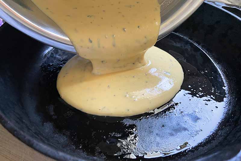 Horizontal image of pouring a thick yellow batter into an oiled pan.