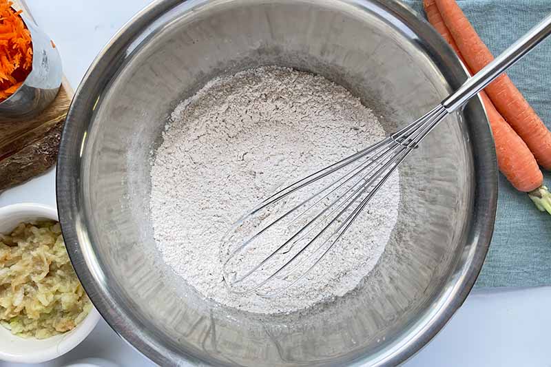 Horizontal image of whisking together dry ingredients in a metal bowl.