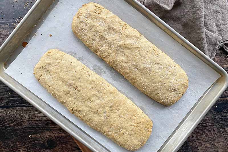 Horizontal image of two large partially baked dough logs on a lined baking sheet.
