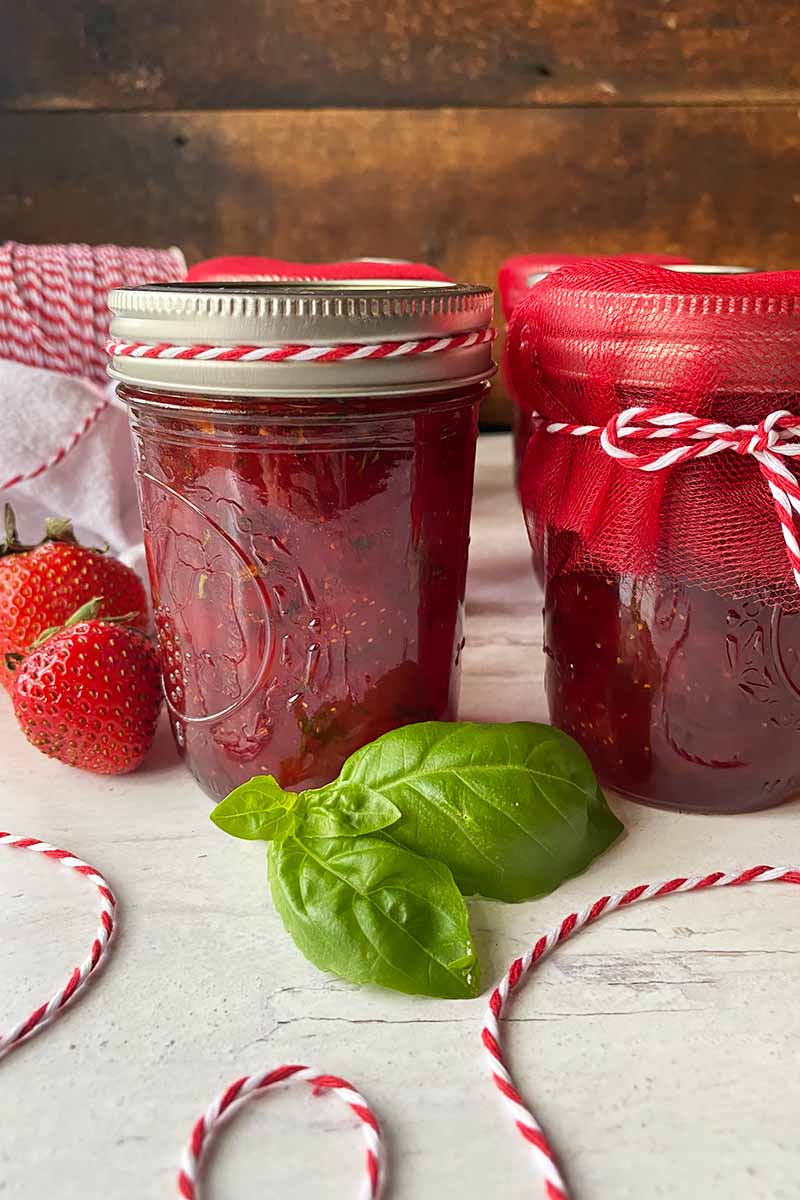 Vertical image of jarred red jelly next to fresh herbs and string.
