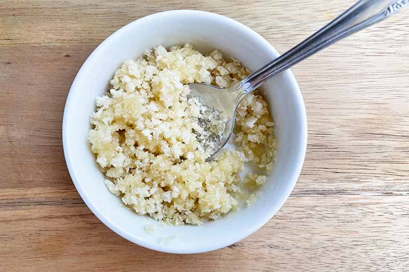 Horizontal image of mixing together butter and breadcrumbs in a small white bowl.