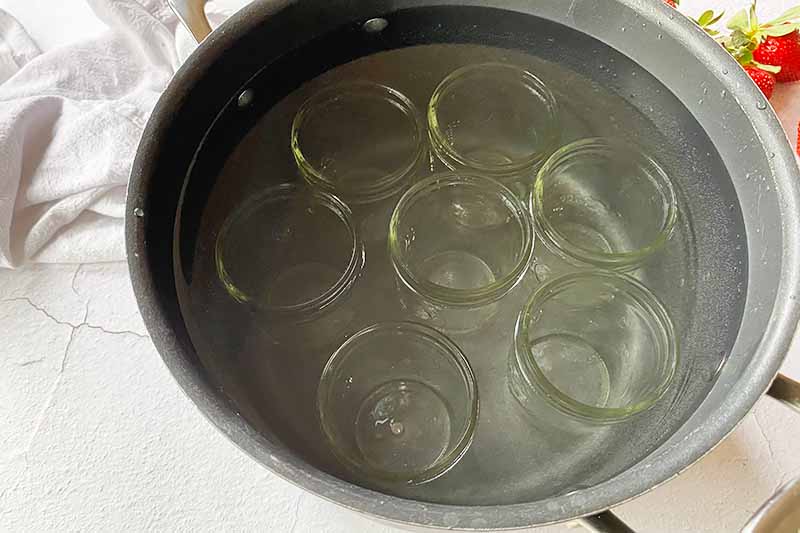 Horizontal image of sanitizing empty glass jars in a pot of water.