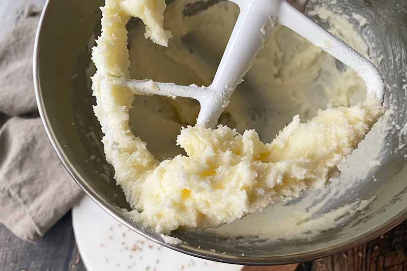 Horizontal image of creamed butter and sugar on a paddle attachment of a stand mixer.