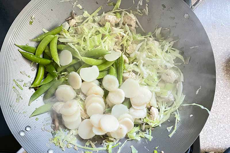 Horizontal image of cooking cabbage slices, peas, and water chestnuts in a wok.