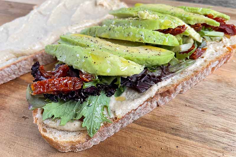 Horizontal image of avocado on top of lettuce on slices of bread.