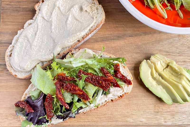 Horizontal image of slices of bread spread with hummus and topped with lettuce and sun-dried tomatoes.