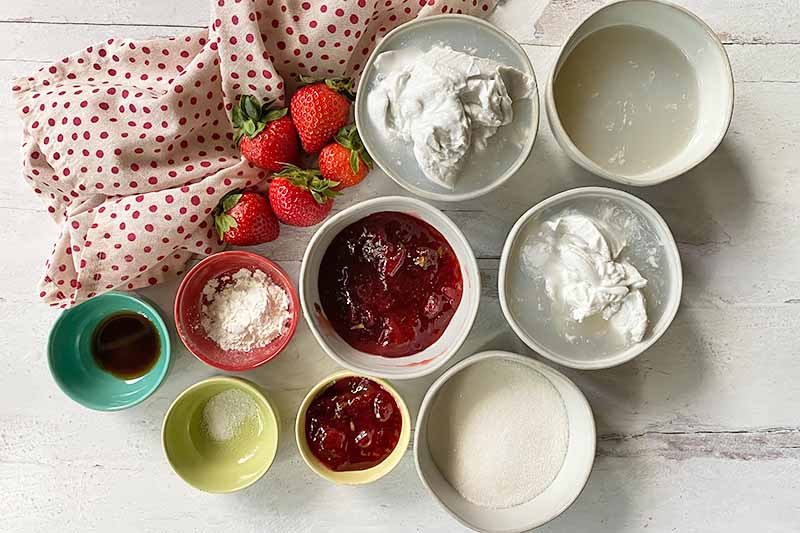 Horizontal image of small bowls filled with prepped wet ingredients next to a polka dot towel and fresh fruit.
