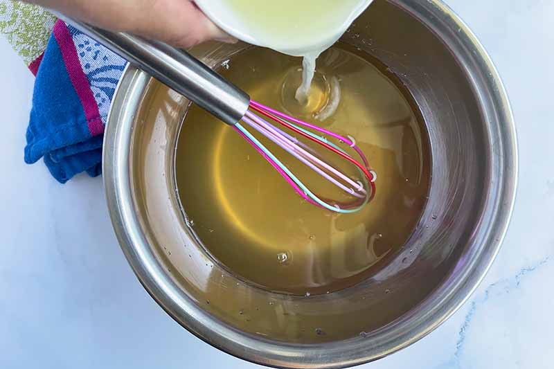 Horizontal image of adding lime into a liquid in a bowl with a whisk.