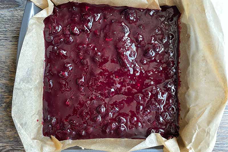 Horizontal image of a blueberry compote in a square pan lined with paper.