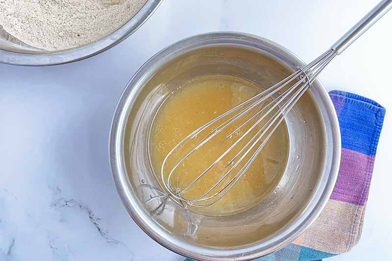 Horizontal image of whisking wet yellow ingredients together in a small metal bowl.