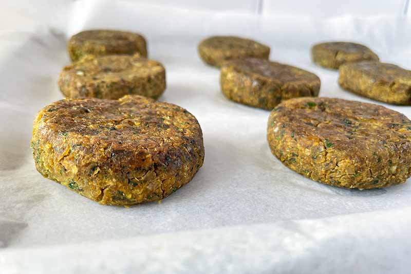 Horizontal image of baked falafel on a baking sheet lined with parchment paper.