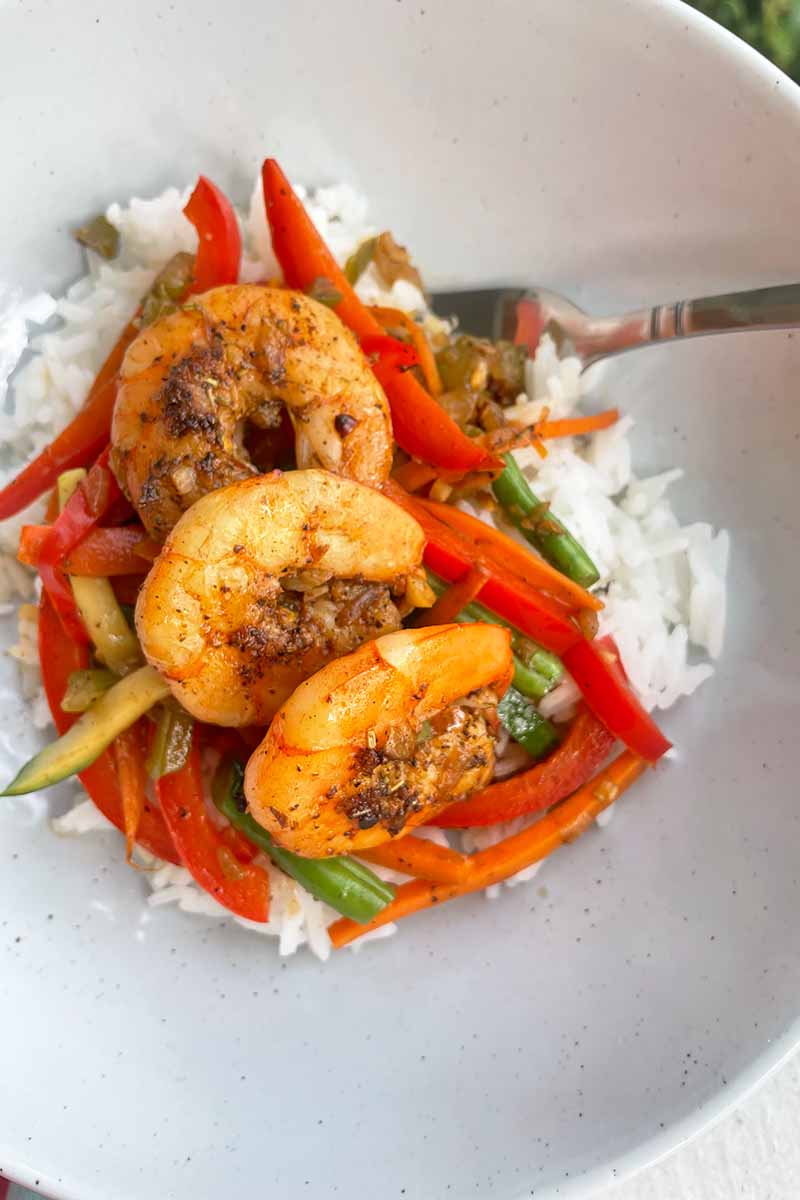 Vertical close-up image of a plated dinner with rice, slices of zucchini and bell peppers, and seafood.