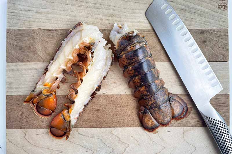 Horizontal image of slicing shell-on seafood in half with a chef's knife on a wooden cutting board.