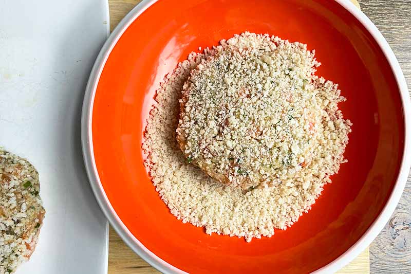 Horizontal image of covering the outside of a patty with panko breadcrumbs in a red plate.