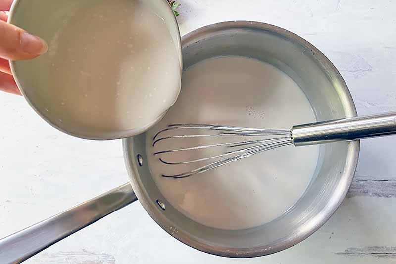 Horizontal image of slowly whisking in slurry in a pot of white liquid.