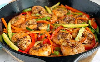 Horizontal image of a cast iron pan filled with cooked sliced zucchini, red bell peppers, and shrimp.