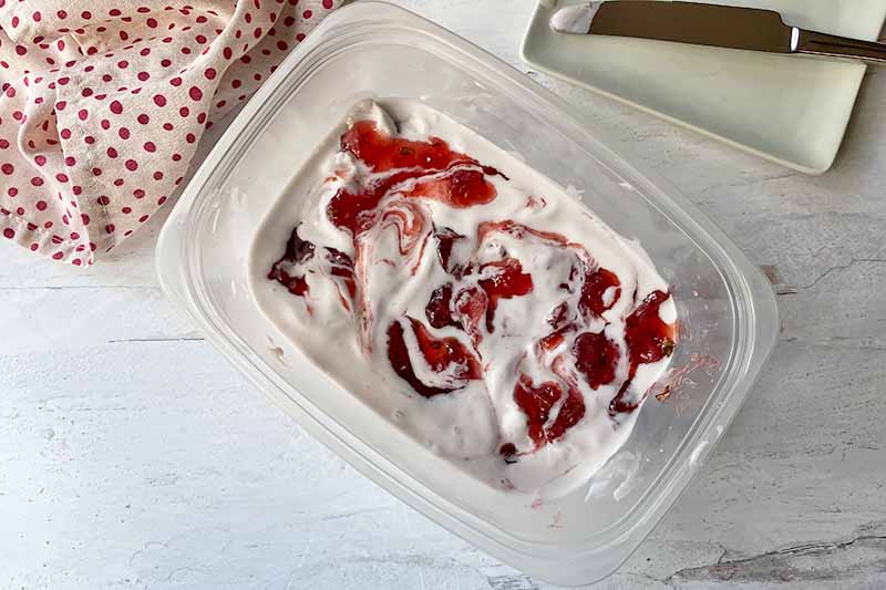 Horizontal image of the top of a frozen dessert in a rectangular container with pink swirls of jelly.