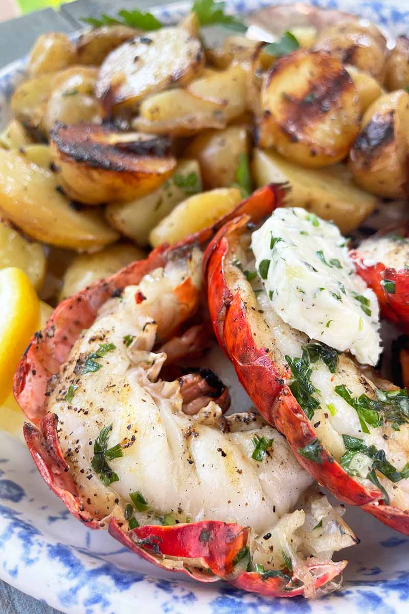 Vertical close-up image of cooked seafood with herbs and butter next to vegetables on a large plate.