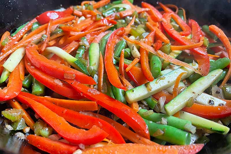 Horizontal image of assorted veggies cooking in a cast iron pan.