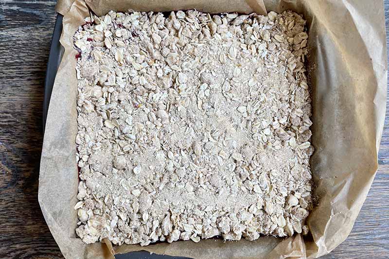 Horizontal image of an unbaked streusel topping in a square pan lined with paper.